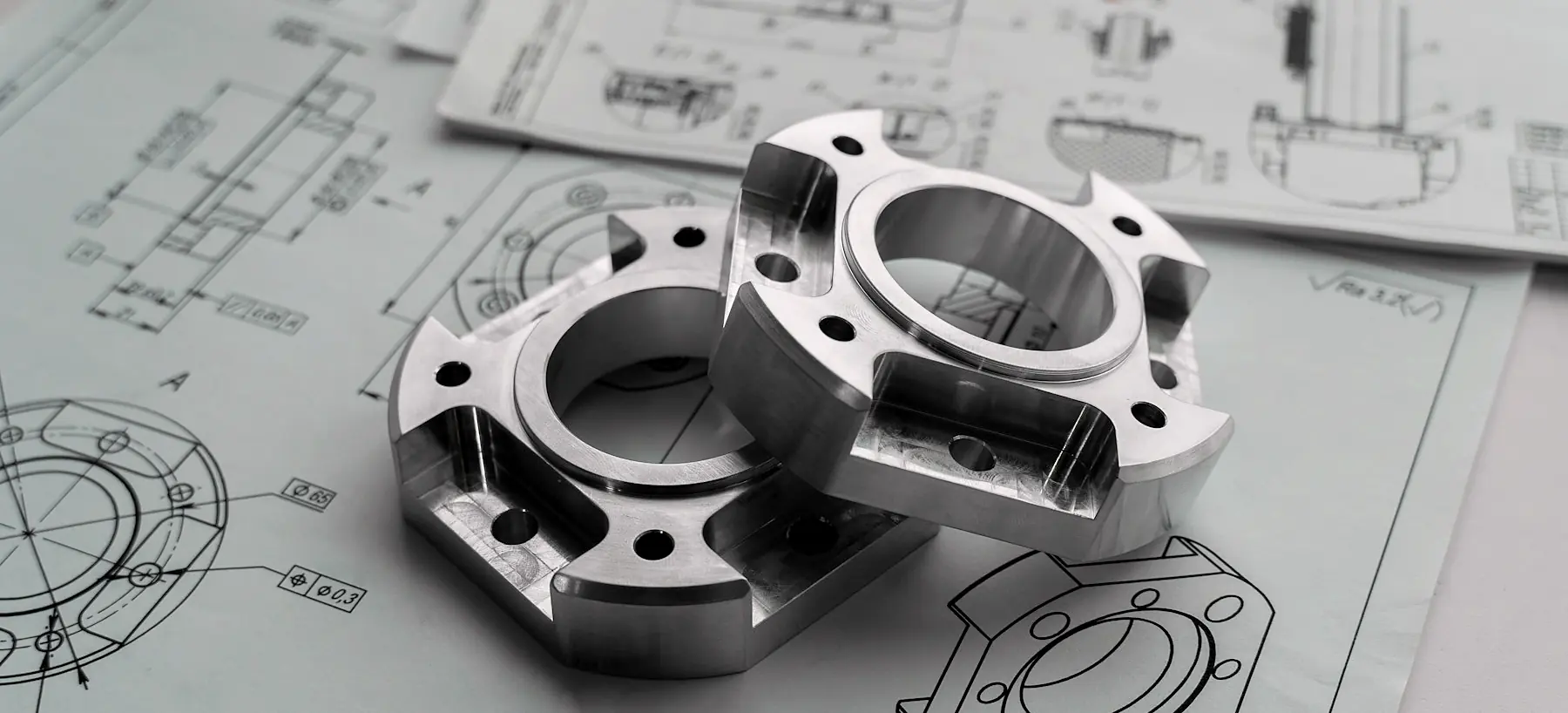 Two machined aluminum flanges resting on printed engineering drawings of the same part
