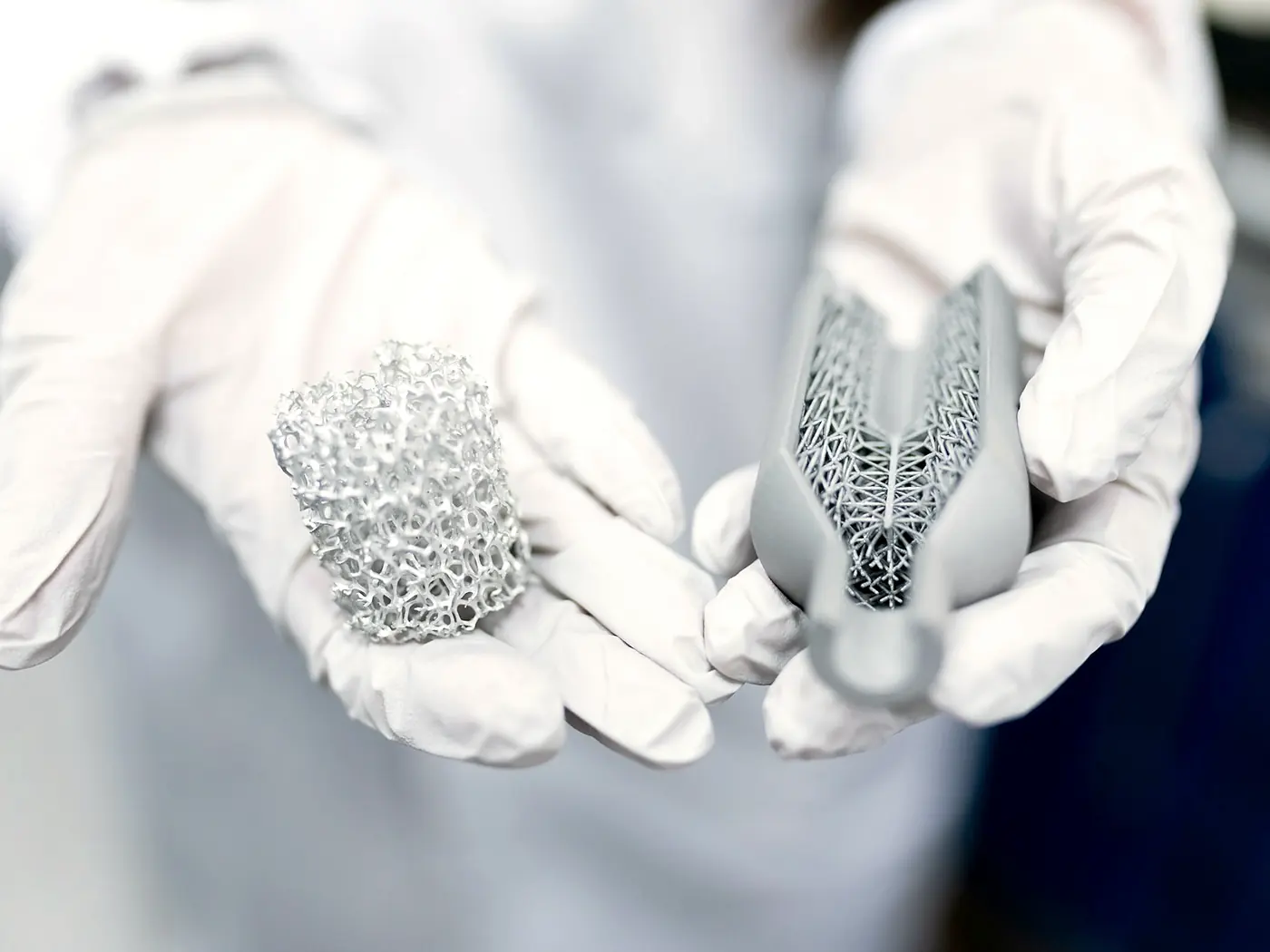 Gloved hands holding two small lattice structured metal parts