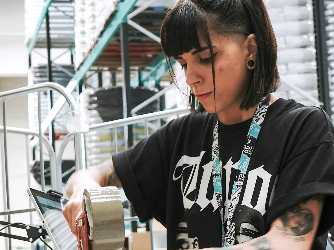 A worker sealing a carton with a tape gun at a packing bench