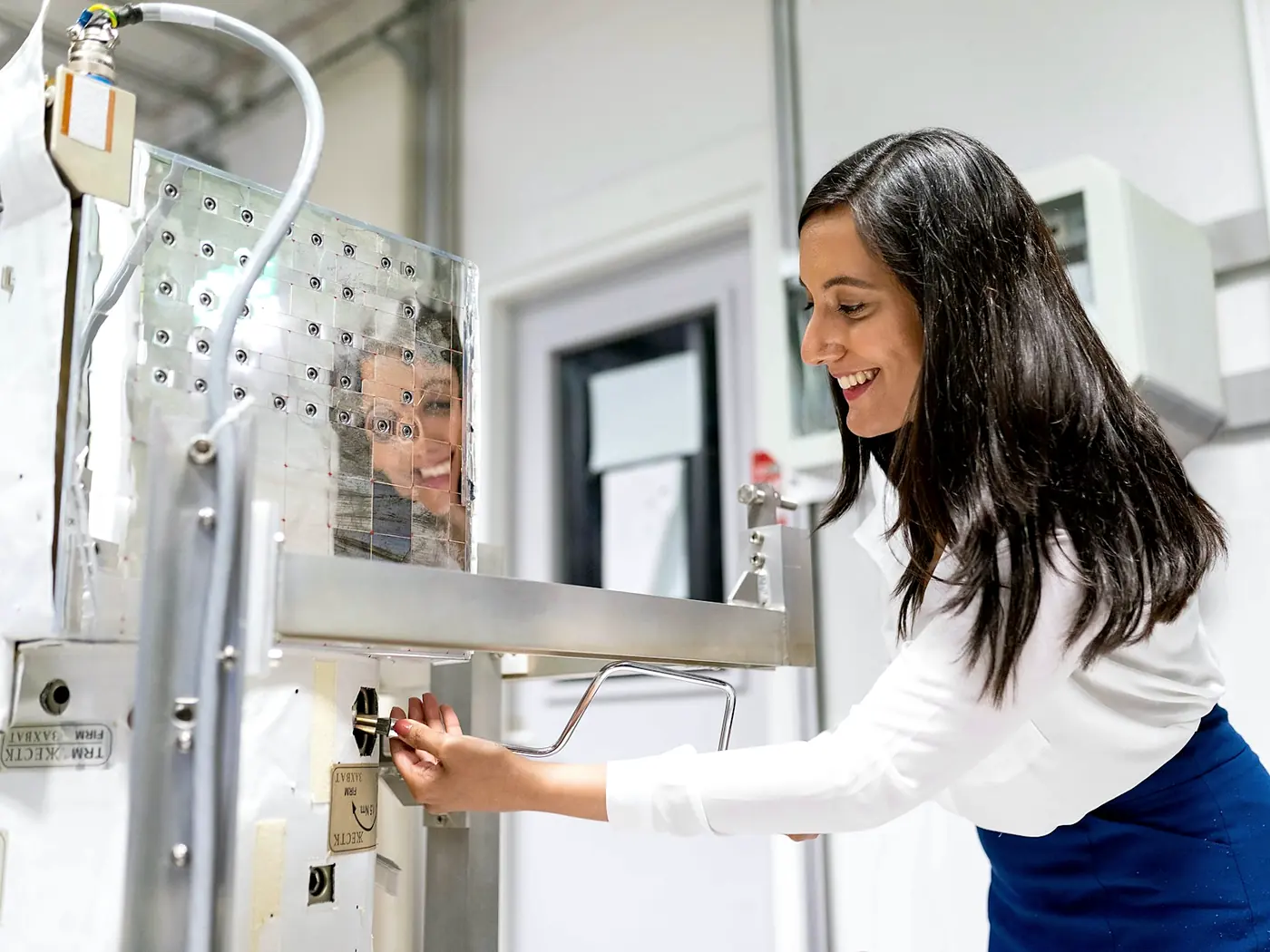 A technician working the door latch of a stainless steel vacuum chamber